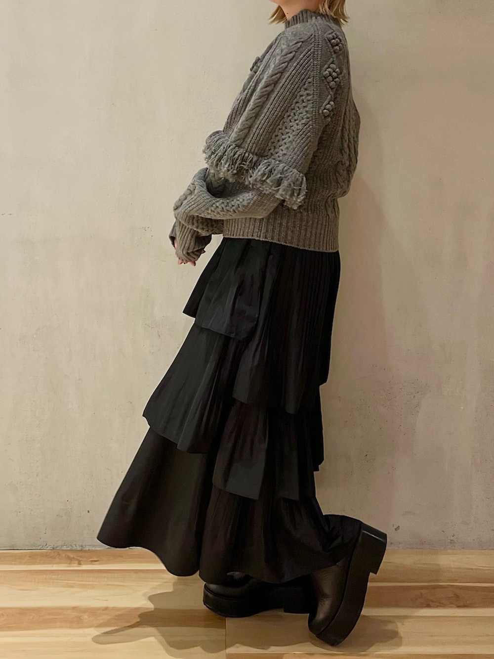 グレー系のニット/セーター、ブラック系のスカート、ブラック系のブーツを着用したレディースの秋コーディネートの2枚目の写真