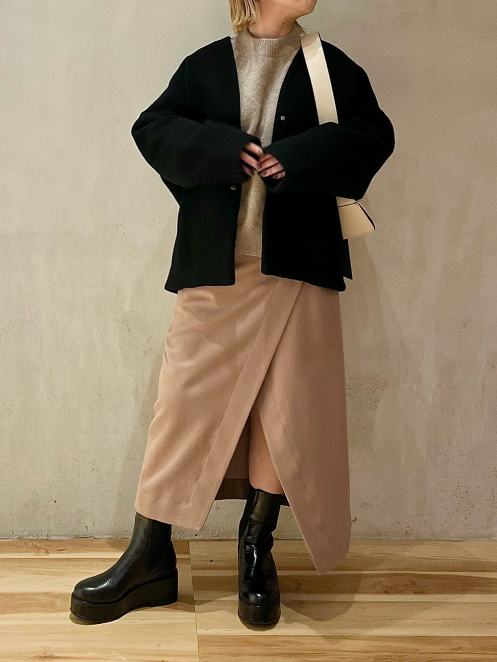 ブラック系のノーカラーコート、ベージュ系のニット/セーター、ベージュ系のスカートを着用したレディースの秋コーディネートの2枚目の写真