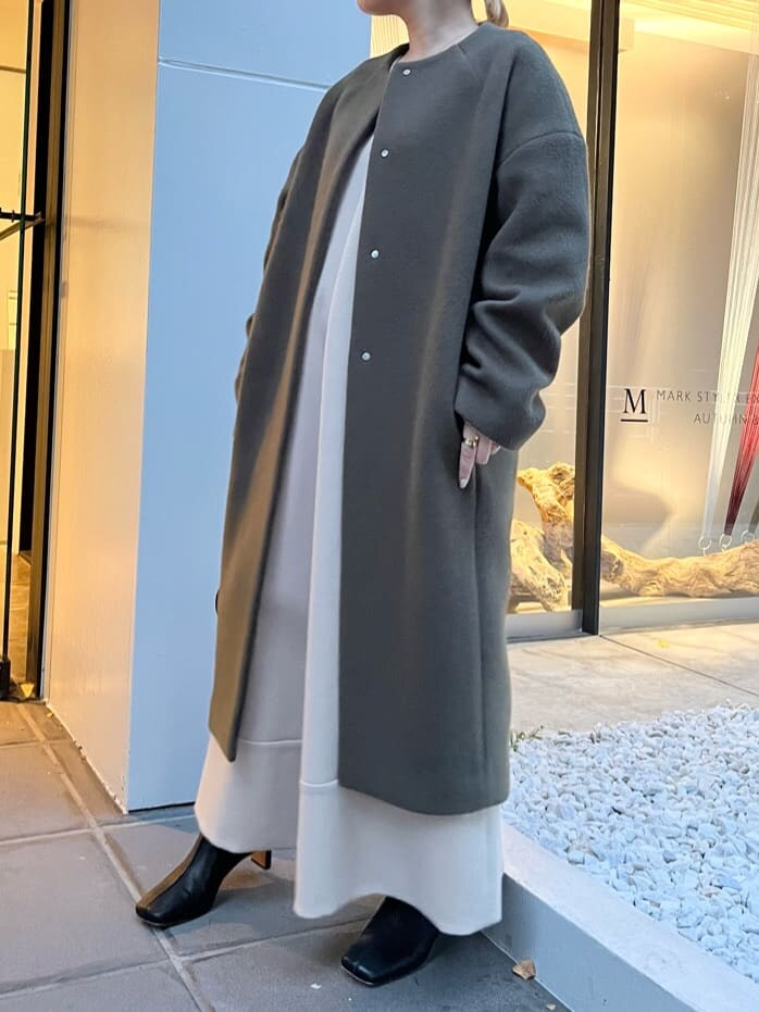 ホワイト系のショルダーバッグ、グリーン系のノーカラーコート、ベージュ系のワンピースを着用したレディースの秋コーディネートの2枚目の写真