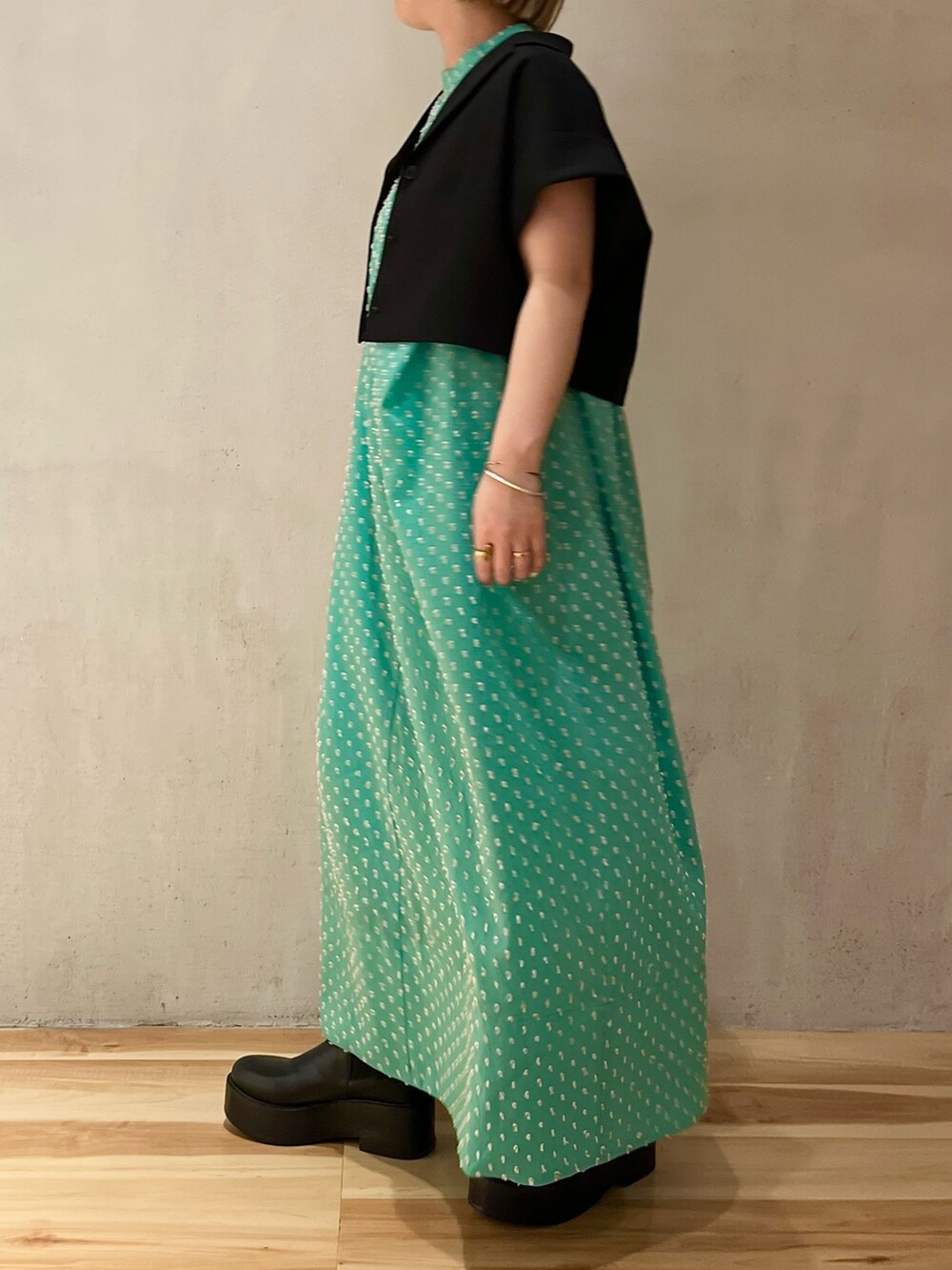 ブラック系のテーラードジャケット、グリーン系のワンピース、ブラック系のブーツを着用したレディースの春コーディネートの2枚目の写真