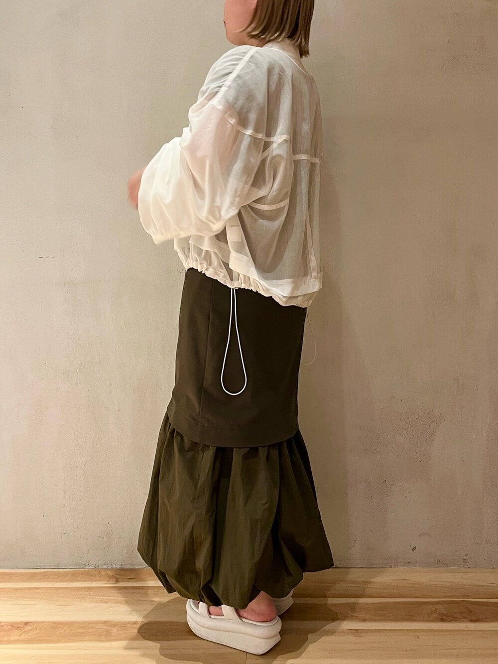 ホワイト系のサンダル、ホワイト系のブルゾン、グリーン系のワンピースを着用したレディースの冬コーディネートの2枚目の写真