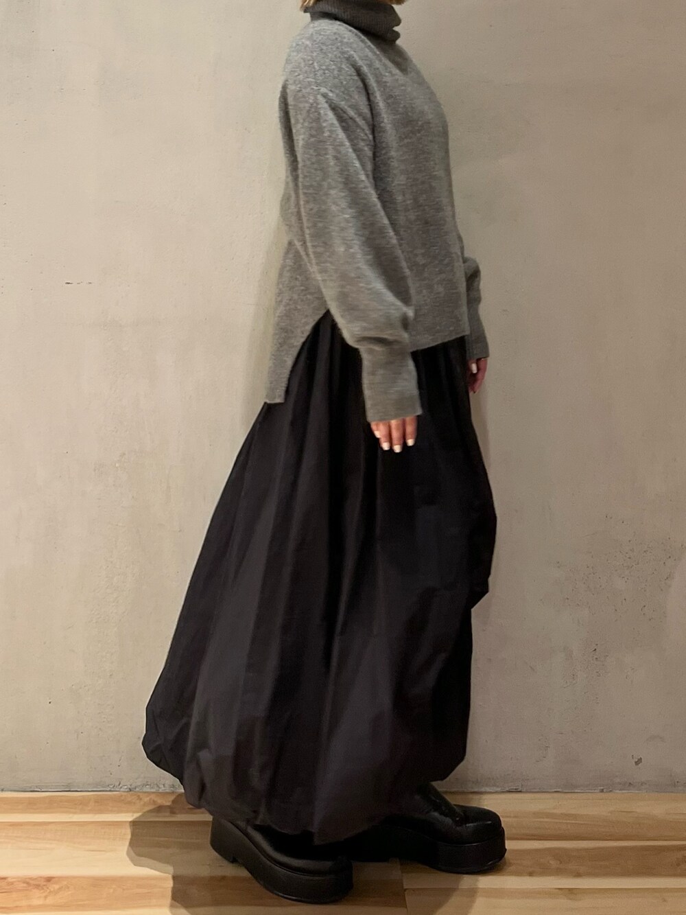 グレー系のニット/セーター、ブラック系のスカート、ブラック系のブーツを着用したレディースの冬コーディネートの6枚目の写真