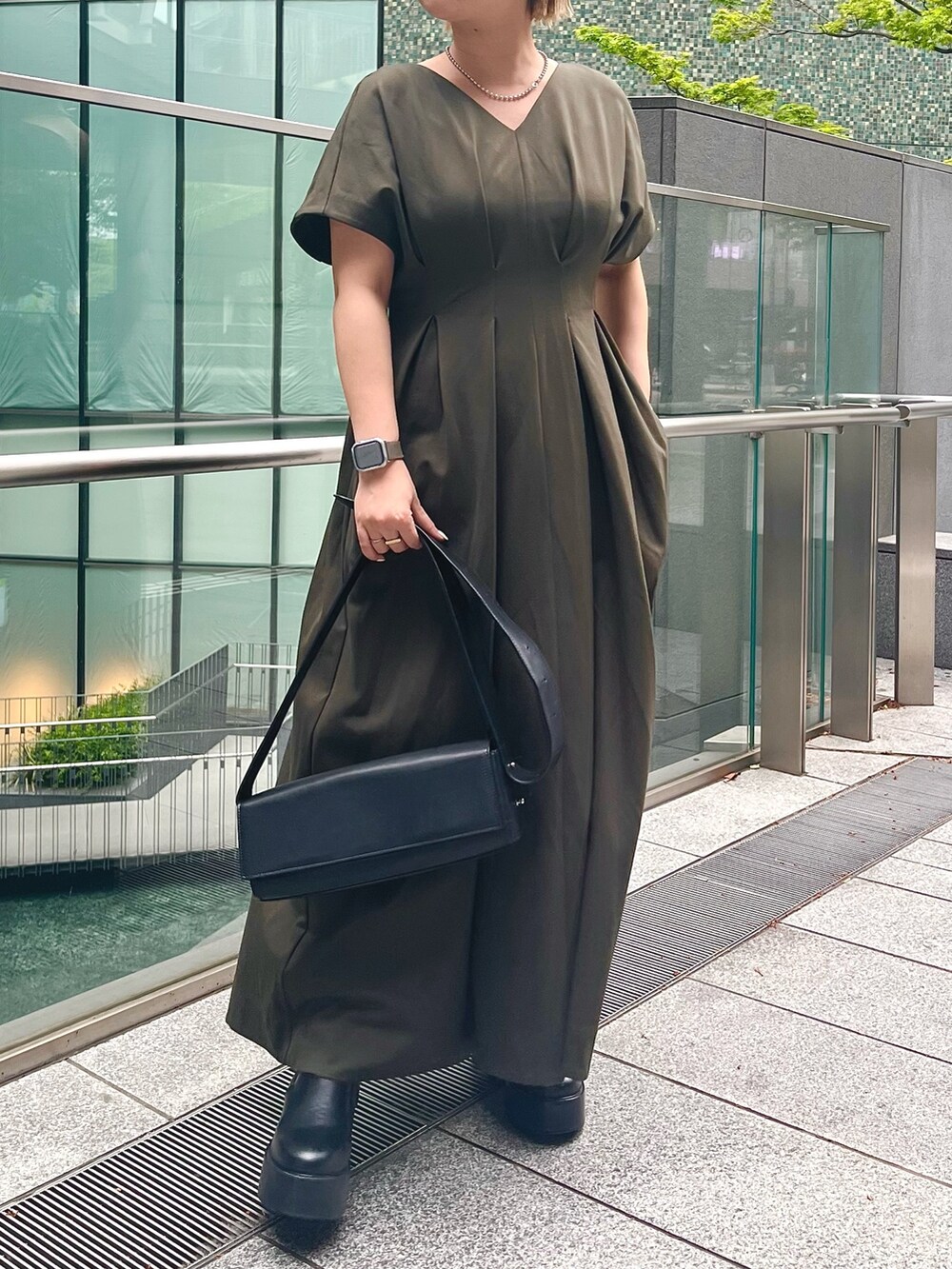 グリーン系のワンピース、ブラック系のブーツ、ブラック系のショルダーバッグを着用したレディースの春コーディネートの2枚目の写真