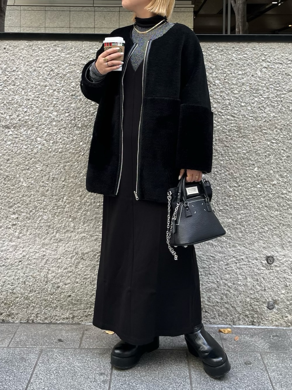 ブラック系のノーカラーコート、シルバー系のTシャツ/カットソー、ブラック系のブーツを着用したレディースの冬コーディネートの2枚目の写真