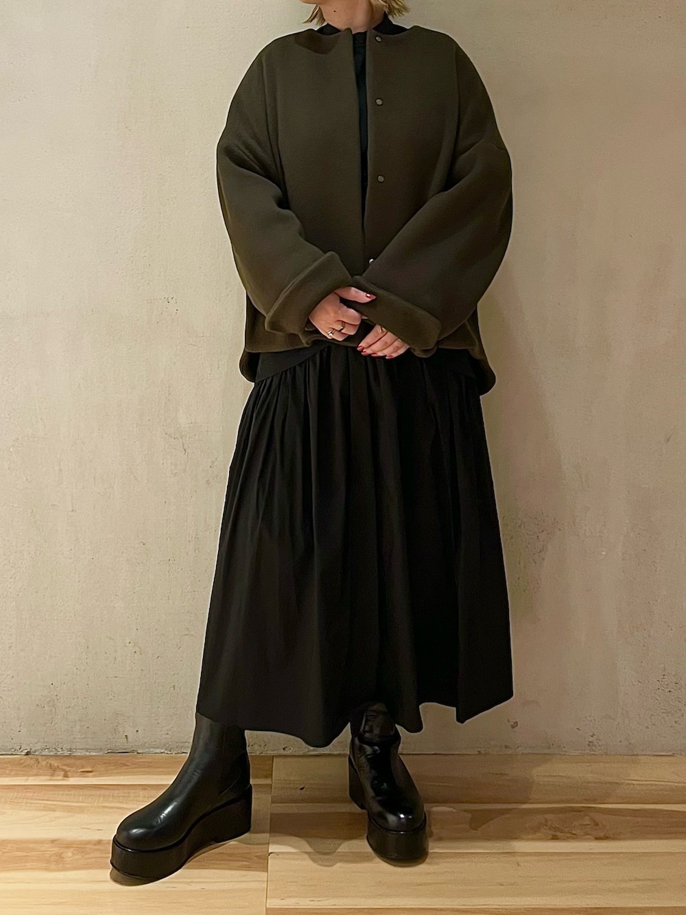 グリーン系のノーカラージャケット、ブラック系のワンピース、ブラック系のブーツを着用したレディースの秋コーディネートの4枚目の写真