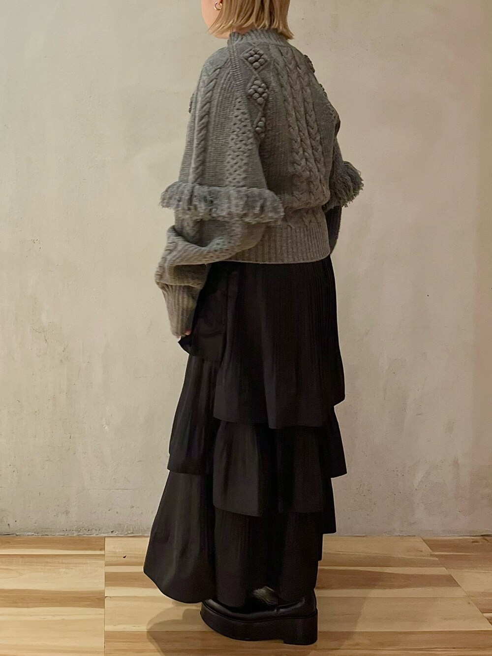 グレー系のニット/セーター、ブラック系のスカート、ブラック系のブーツを着用したレディースの秋コーディネートの4枚目の写真