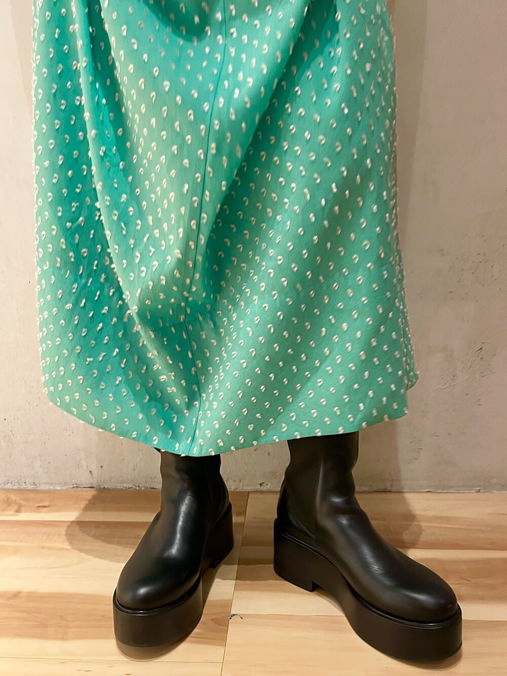 ブラック系のテーラードジャケット、グリーン系のワンピース、ブラック系のブーツを着用したレディースの春コーディネートの8枚目の写真