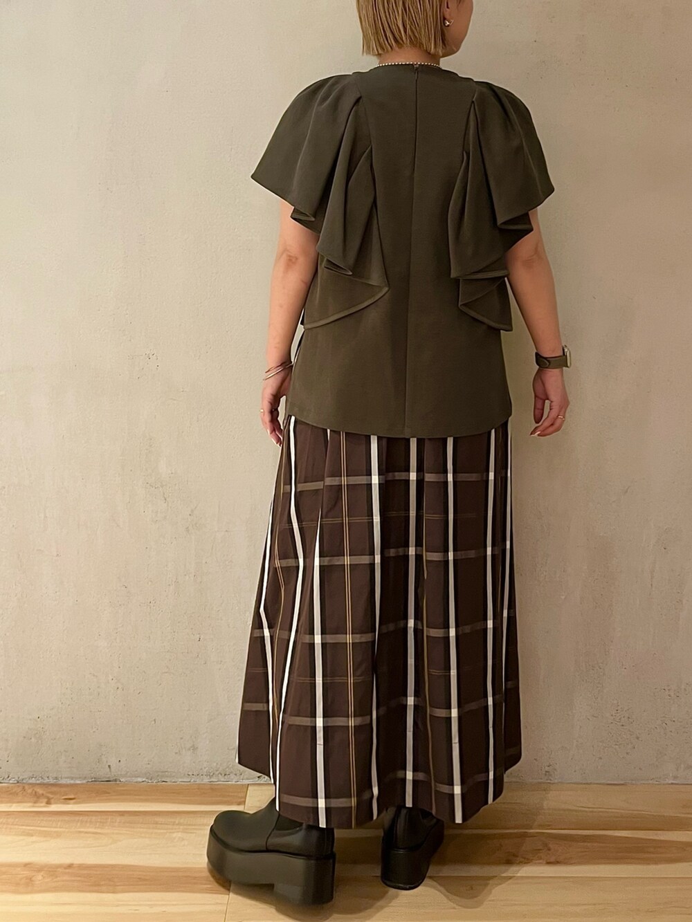 ブラック系のブーツ、グリーン系のTシャツ/カットソー、ブラウン系のスカートを着用したレディースの春コーディネートの3枚目の写真