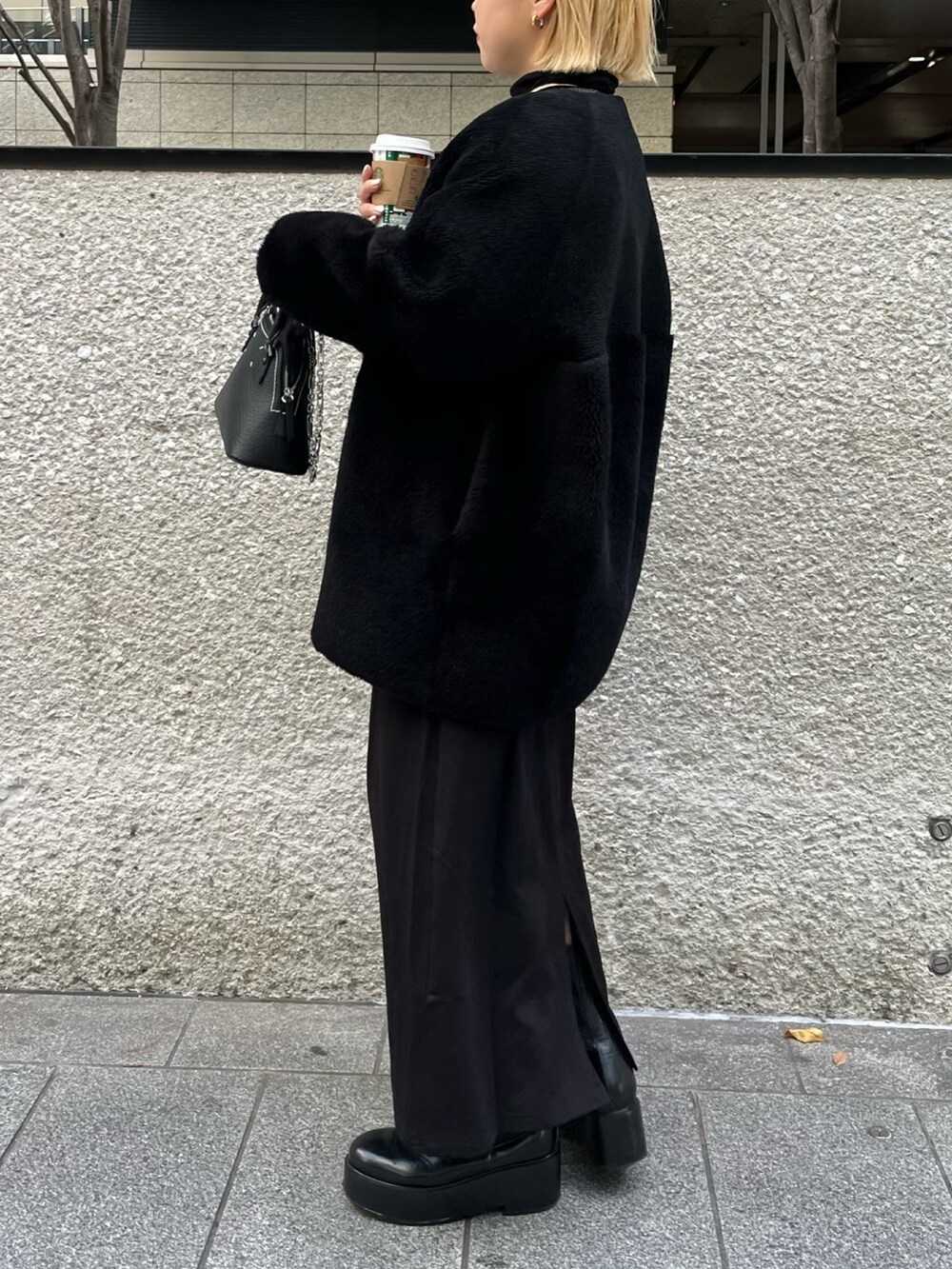 ブラック系のノーカラーコート、シルバー系のTシャツ/カットソー、ブラック系のブーツを着用したレディースの冬コーディネートの3枚目の写真