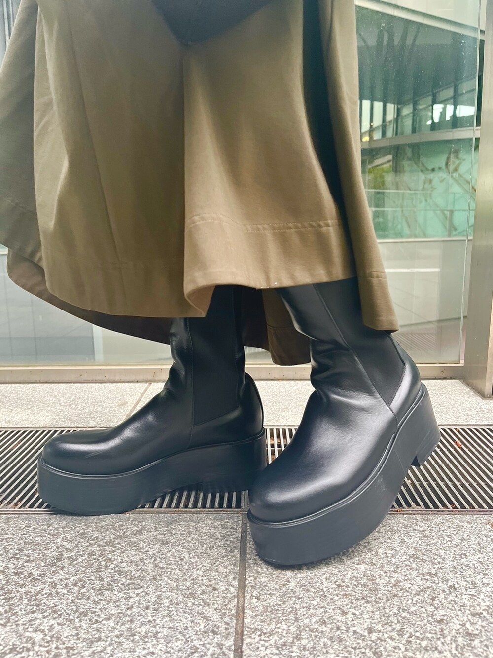 グリーン系のワンピース、ブラック系のブーツ、ブラック系のショルダーバッグを着用したレディースの春コーディネートの8枚目の写真