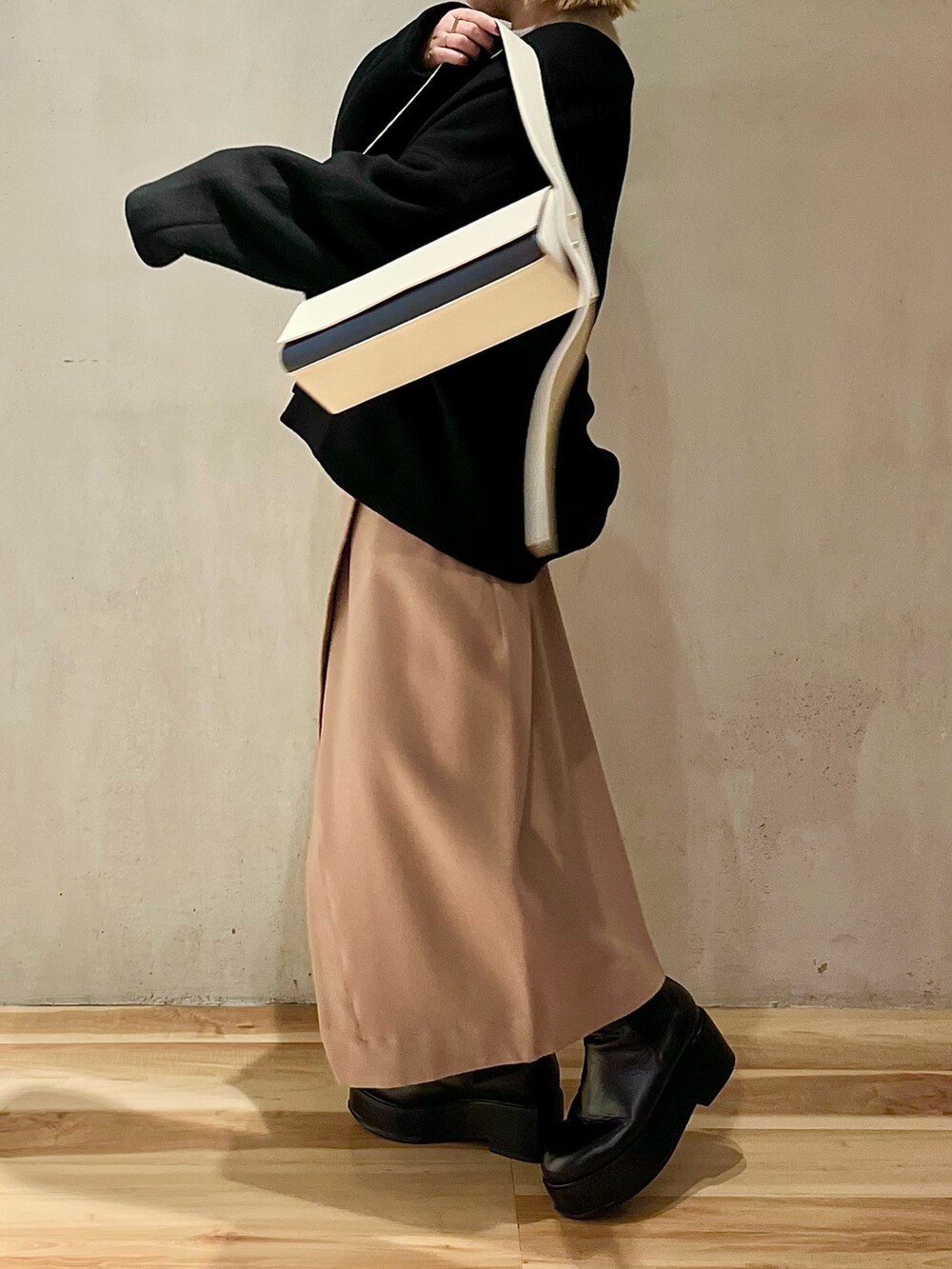 ブラック系のノーカラーコート、ベージュ系のニット/セーター、ベージュ系のスカートを着用したレディースの秋コーディネートの3枚目の写真