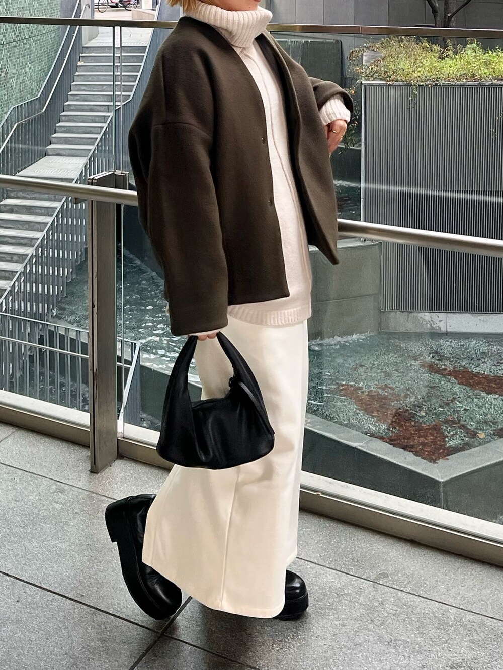 グリーン系のノーカラーコート、ブラック系のブーツを着用したレディースの冬コーディネートの2枚目の写真