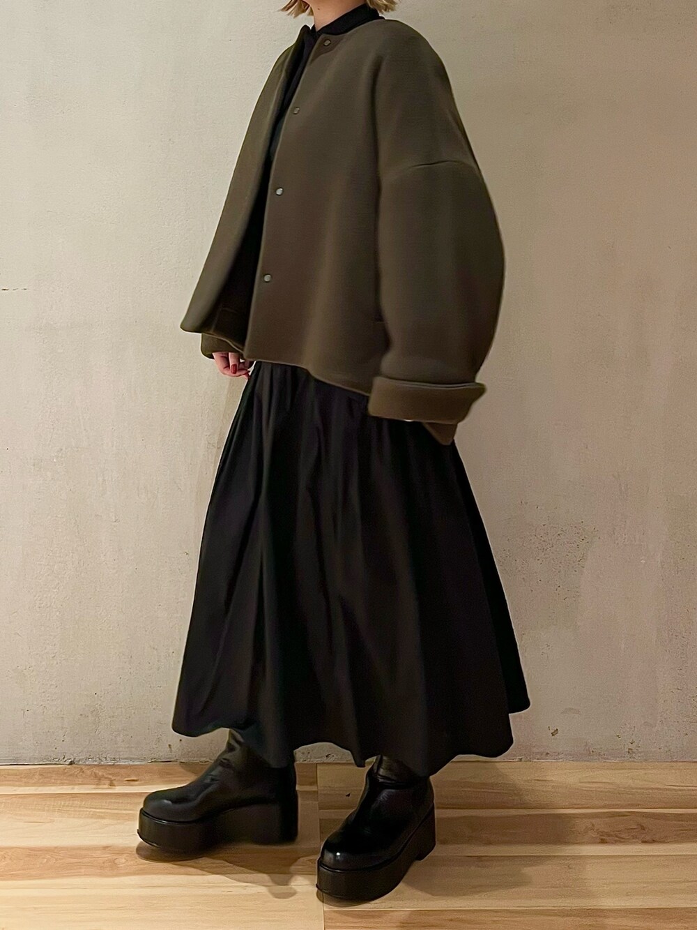 グリーン系のノーカラージャケット、ブラック系のワンピース、ブラック系のブーツを着用したレディースの秋コーディネートの2枚目の写真