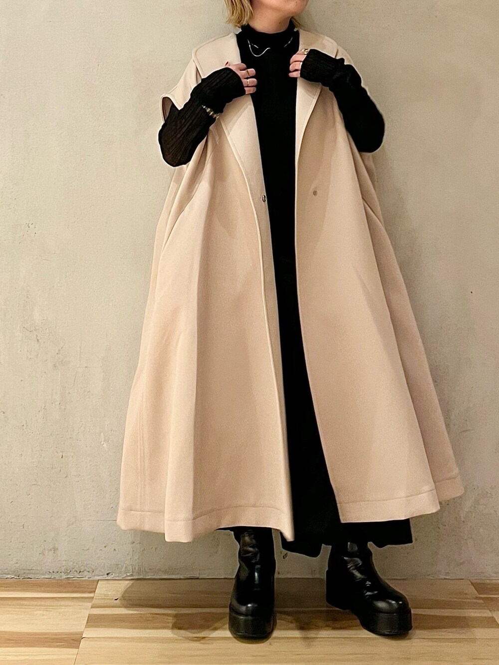 ベージュ系のノーカラーコート、ブラック系のニット/セーター、ブラック系のブーツを着用したレディースの秋コーディネートの3枚目の写真