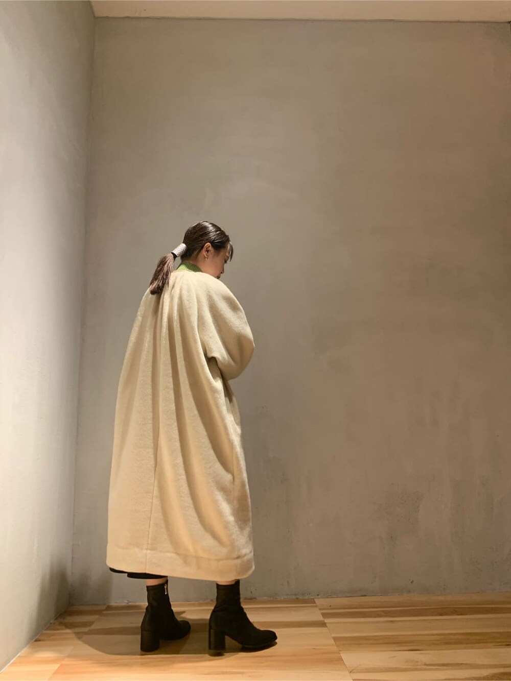 ブラック系のスカート、グリーン系のニット/セーター、ベージュ系のノーカラーコートを着用したレディースの秋コーディネートの2枚目の写真