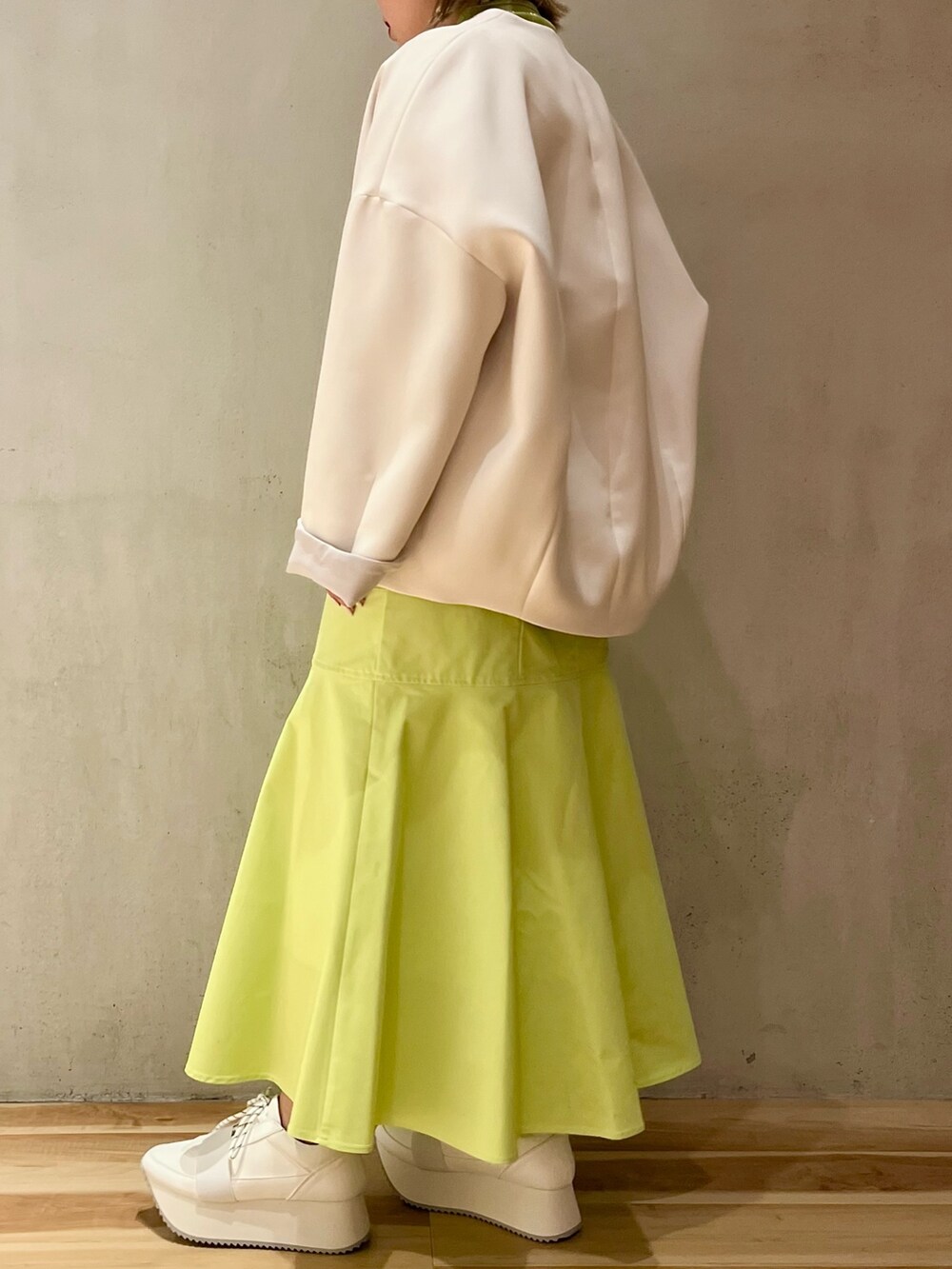 ベージュ系のノーカラーコート、グリーン系のニット/セーター、ベージュ系のショルダーバッグを着用したレディースの冬コーディネートの2枚目の写真