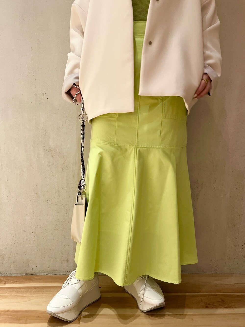 ベージュ系のノーカラーコート、グリーン系のニット/セーター、ベージュ系のショルダーバッグを着用したレディースの冬コーディネートの6枚目の写真