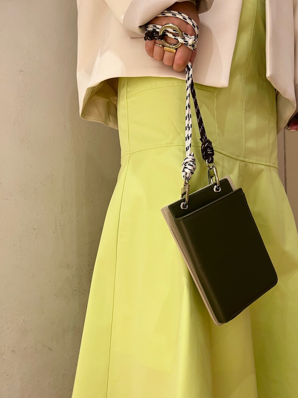 ベージュ系のノーカラーコート、グリーン系のニット/セーター、ベージュ系のショルダーバッグを着用したレディースの冬コーディネートの7枚目の写真