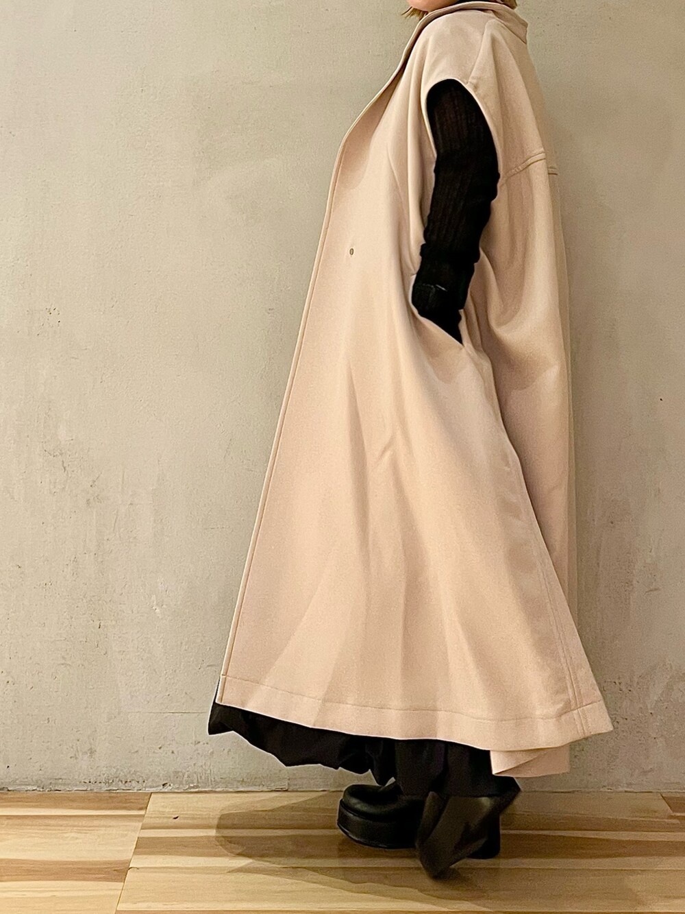 ベージュ系のノーカラーコート、ブラック系のニット/セーター、ブラック系のブーツを着用したレディースの秋コーディネートの2枚目の写真