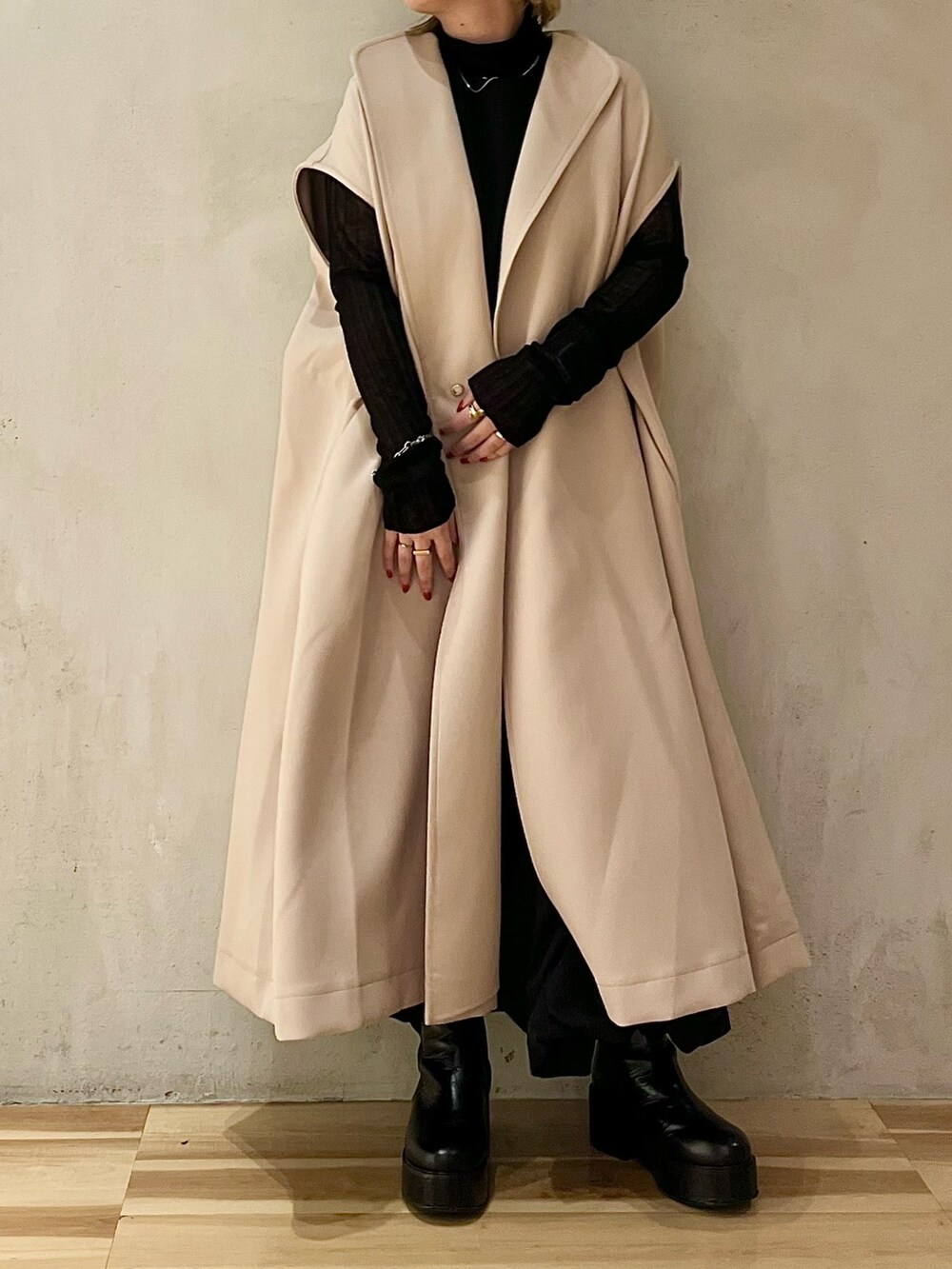 ベージュ系のノーカラーコート、ブラック系のニット/セーター、ブラック系のブーツを着用したレディースの秋コーディネートの4枚目の写真