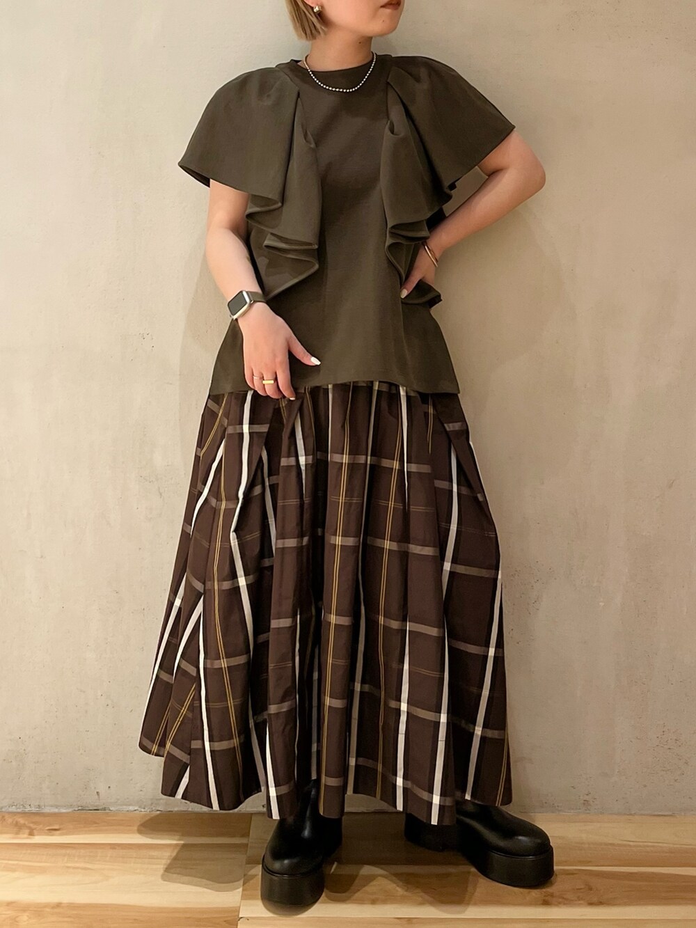 ブラック系のブーツ、グリーン系のTシャツ/カットソー、ブラウン系のスカートを着用したレディースの春コーディネートの2枚目の写真