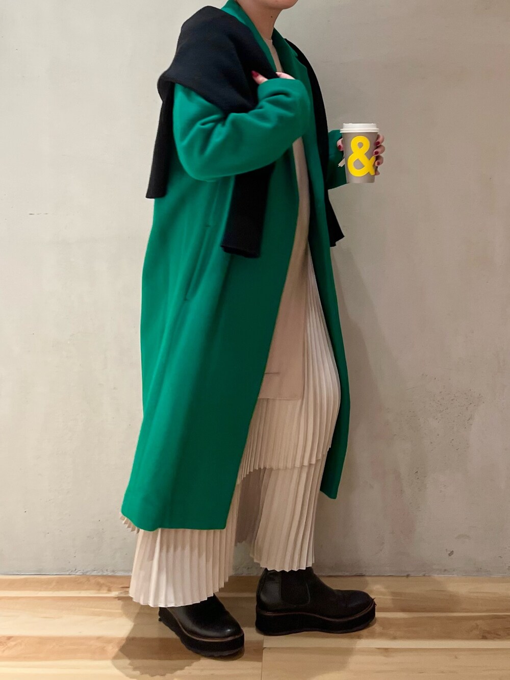 グリーン系のチェスターコート、ブラック系のカーディガン/ボレロ、ベージュ系のワンピースを着用したレディースの冬コーディネートの2枚目の写真