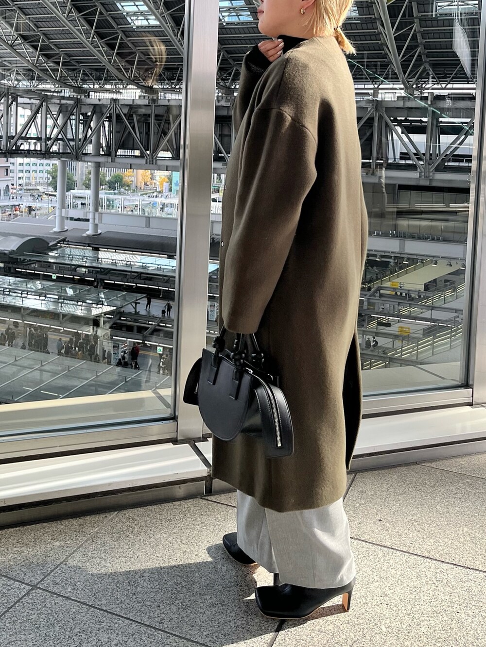 グリーン系のノーカラーコート、グレー系のその他パンツ、ブラック系のハンドバッグを着用したレディースの冬コーディネートの4枚目の写真