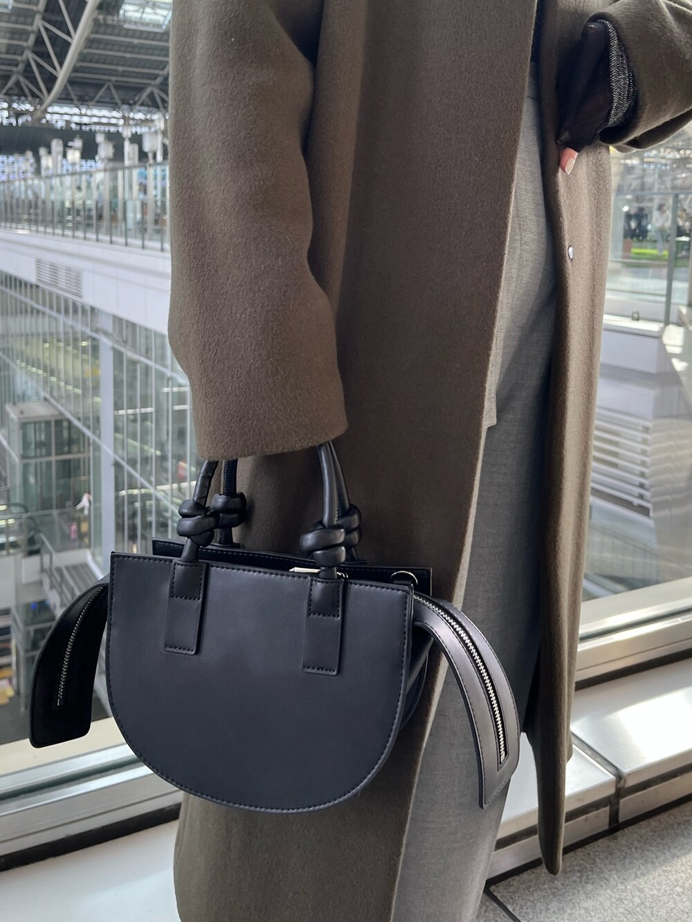 グリーン系のノーカラーコート、グレー系のその他パンツ、ブラック系のハンドバッグを着用したレディースの冬コーディネートの8枚目の写真