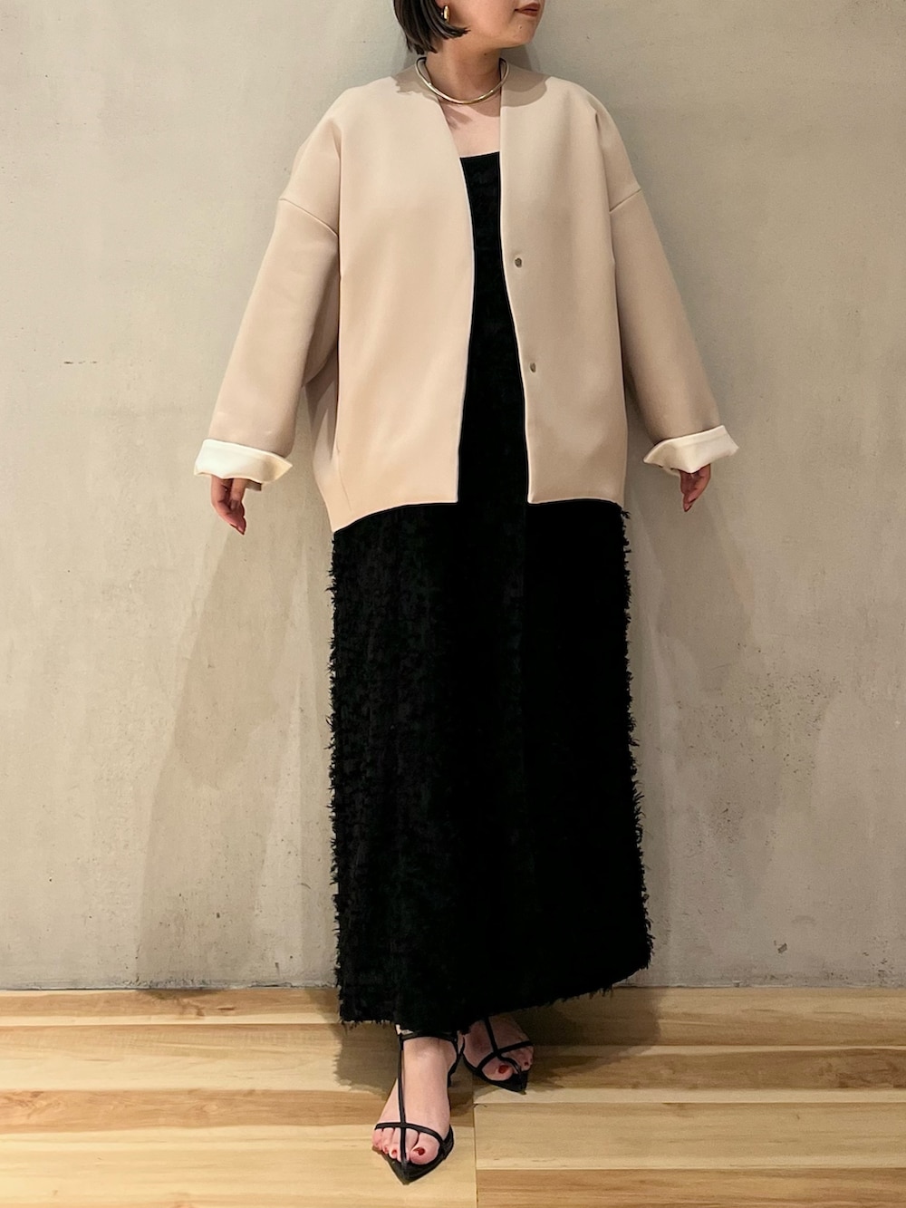 ブラック系のワンピース、ブラック系のタンクトップ、ベージュ系のノーカラーコートを着用したレディースの春コーディネートの2枚目の写真