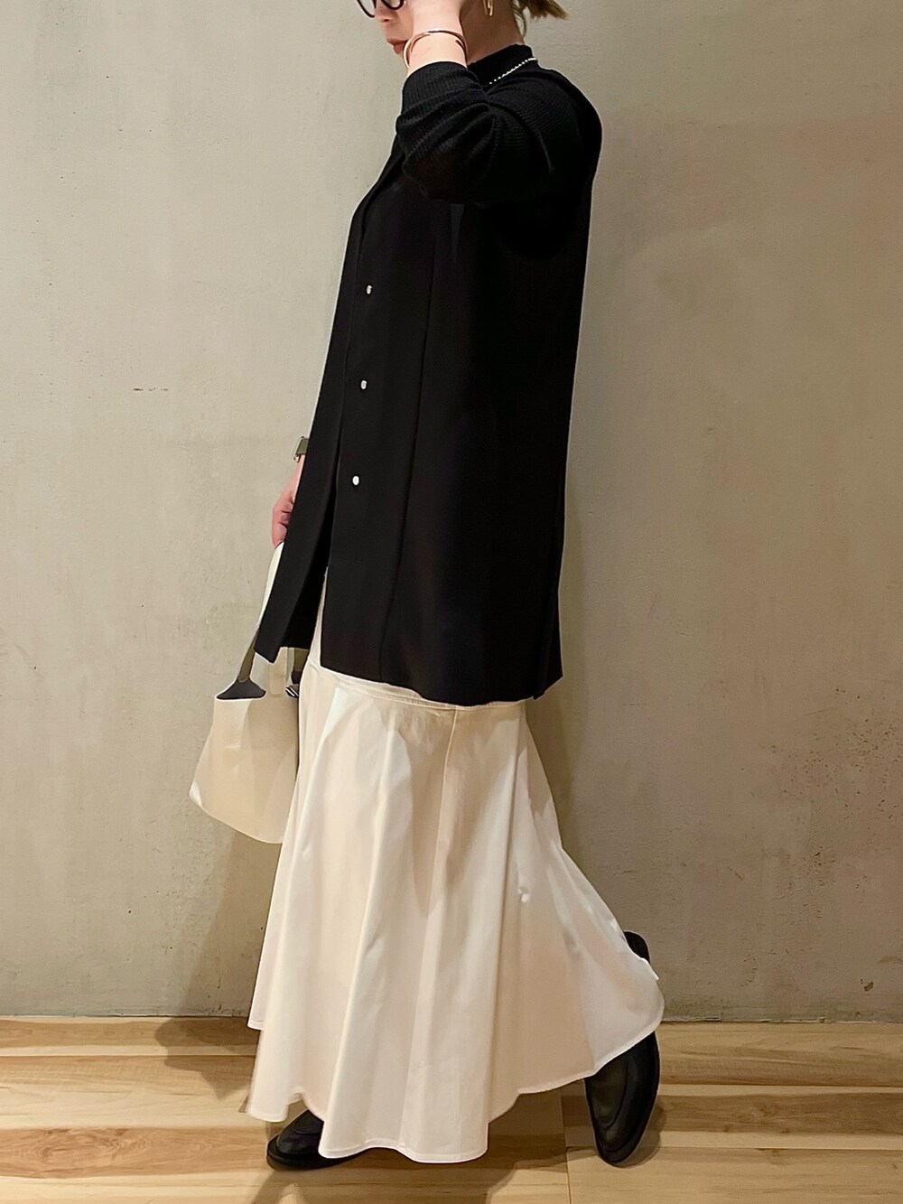 ホワイト系のスカート、ホワイト系のハンドバッグ、ブラック系のテーラードジャケットを着用したレディースの冬コーディネートの2枚目の写真