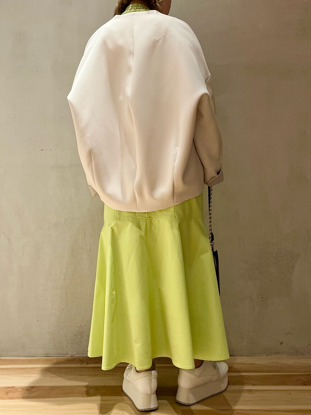 ベージュ系のノーカラーコート、グリーン系のニット/セーター、ベージュ系のショルダーバッグを着用したレディースの冬コーディネートの3枚目の写真