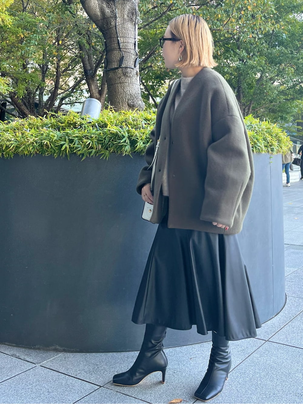 ブラック系のスカート、ブラック系のブーツ、グリーン系のノーカラーコートを着用したレディースの秋コーディネートの2枚目の写真