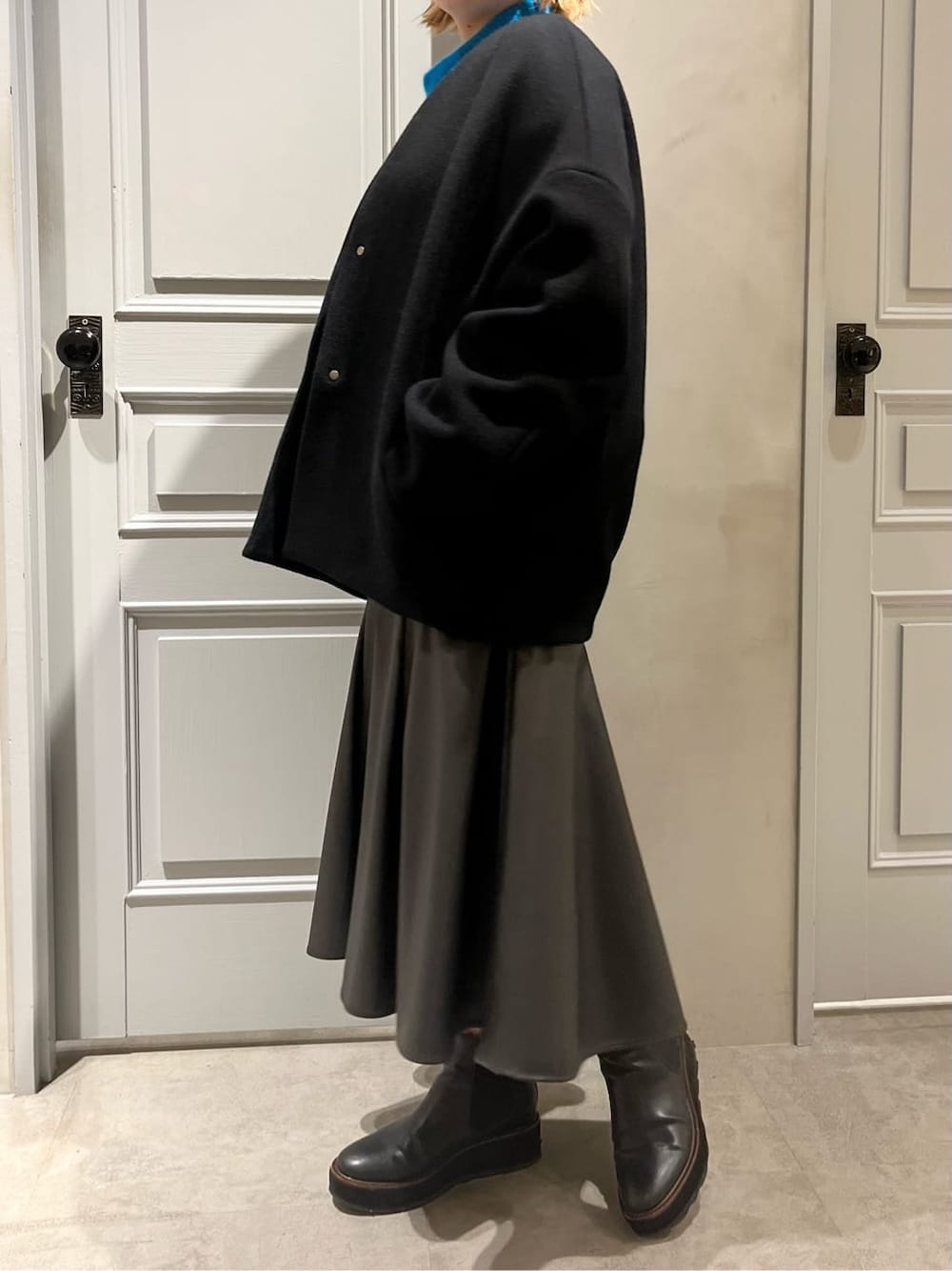 ブラック系のスカート、ブラック系のノーカラーコート、ブルー系のニット/セーターを着用したレディースの秋コーディネートの2枚目の写真