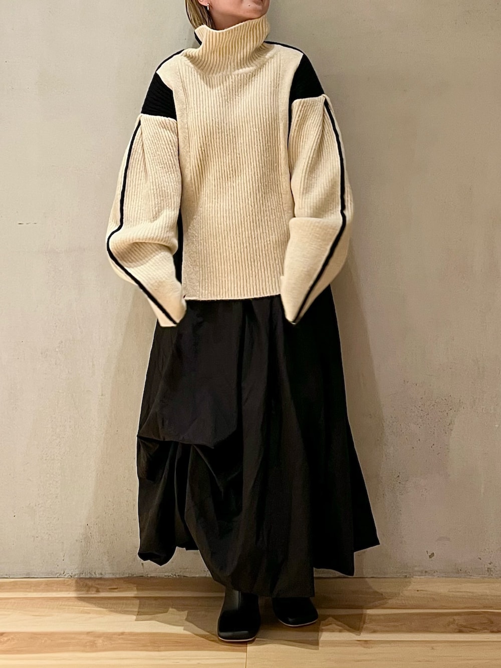 ブラック系のスカート、ホワイト系のニット/セーター、ブラック系のブーツを着用したレディースの秋コーディネートの2枚目の写真