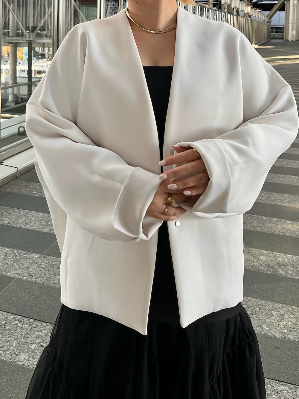 ベージュ系のノーカラーコート、ブラック系のタンクトップ、ブラック系のスカートを着用したレディースの冬コーディネートの6枚目の写真