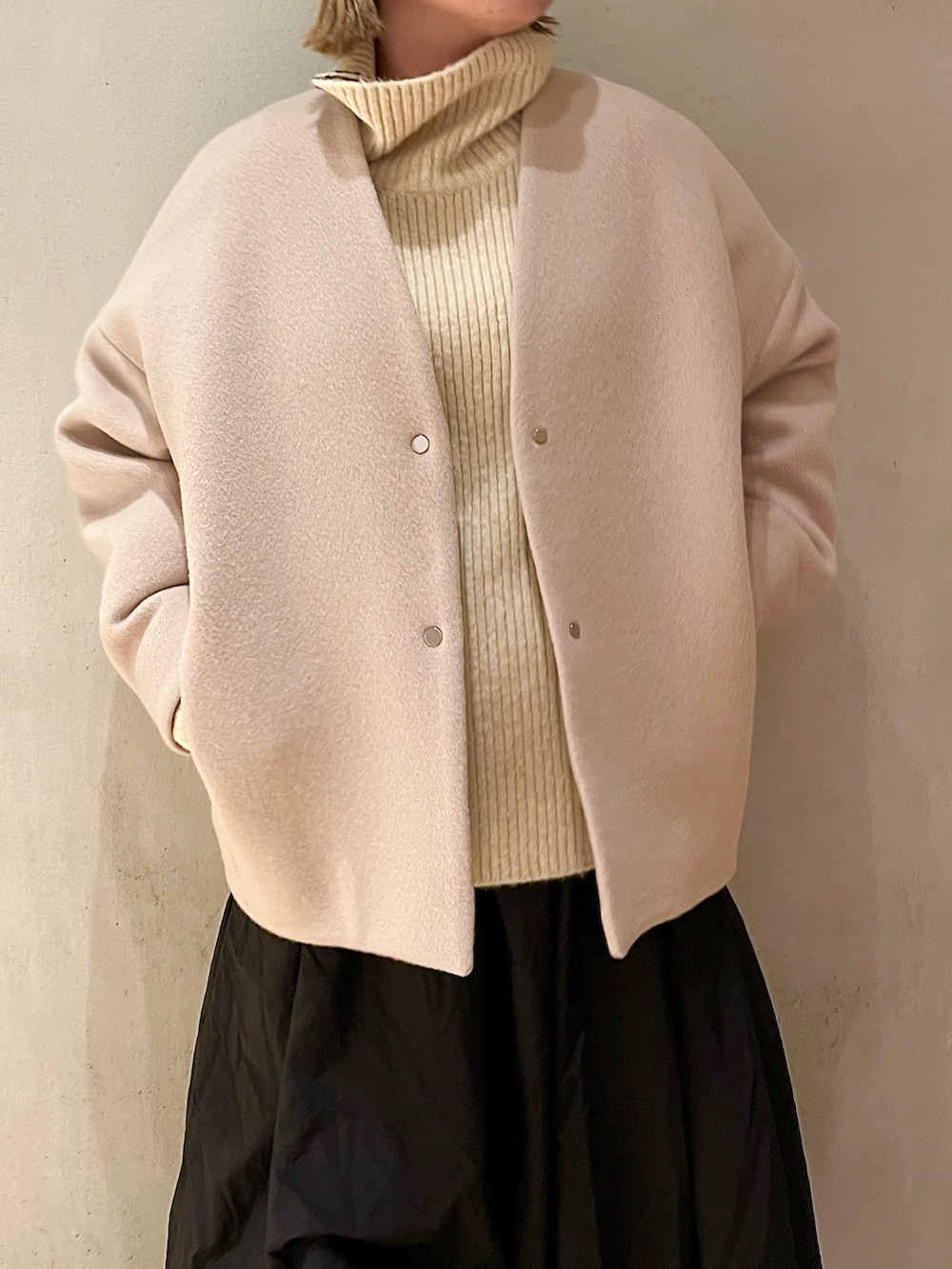 ベージュ系のノーカラーコート、ブラック系のスカート、ブラック系のブーツを着用したレディースの夏コーディネートの5枚目の写真