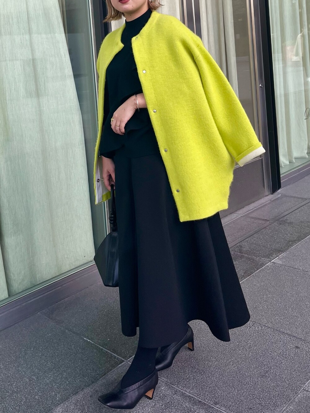イエロー系のカーディガン/ボレロ、ブラック系のニット/セーター、ブラック系のスカートを着用したレディースの冬コーディネートの2枚目の写真
