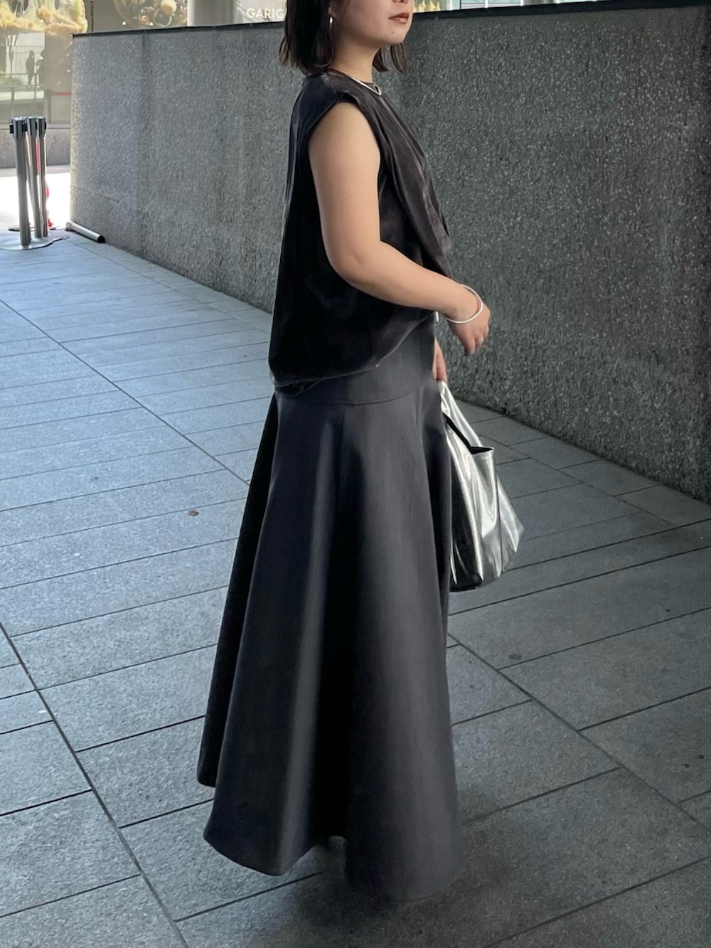 グレー系のスカート、ゴールド系のハンドバッグ、グレー系のTシャツ/カットソーを着用したレディースの夏コーディネートの2枚目の写真