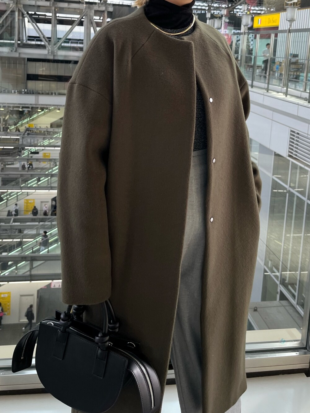 グリーン系のノーカラーコート、グレー系のその他パンツ、ブラック系のハンドバッグを着用したレディースの冬コーディネートの6枚目の写真