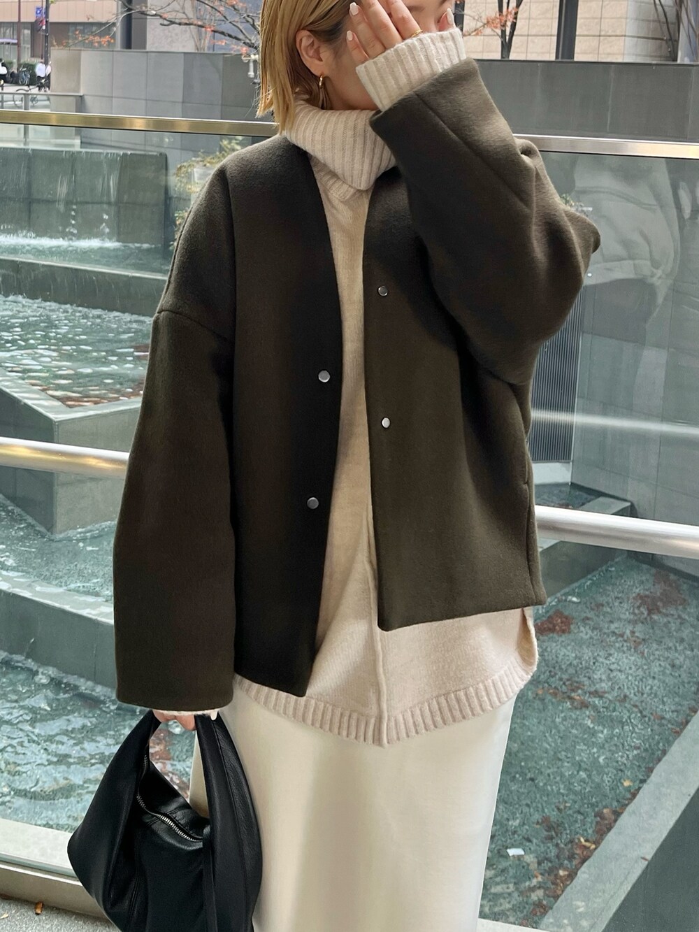 グリーン系のノーカラーコート、ブラック系のブーツを着用したレディースの冬コーディネートの5枚目の写真