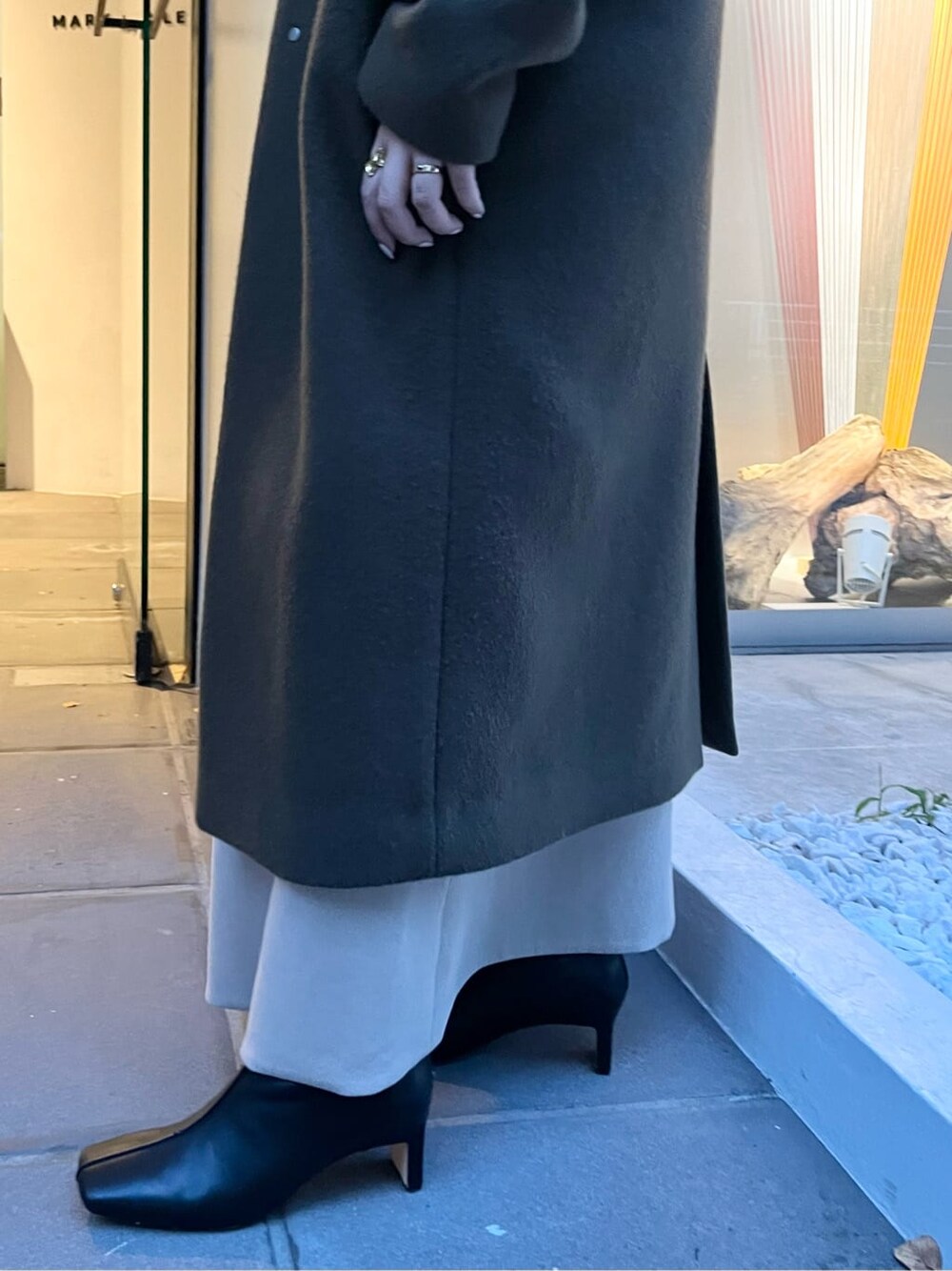 ホワイト系のショルダーバッグ、グリーン系のノーカラーコート、ベージュ系のワンピースを着用したレディースの秋コーディネートの6枚目の写真