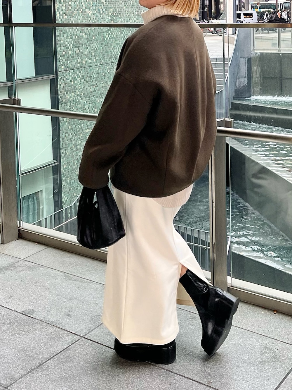 グリーン系のノーカラーコート、ブラック系のブーツを着用したレディースの冬コーディネートの3枚目の写真