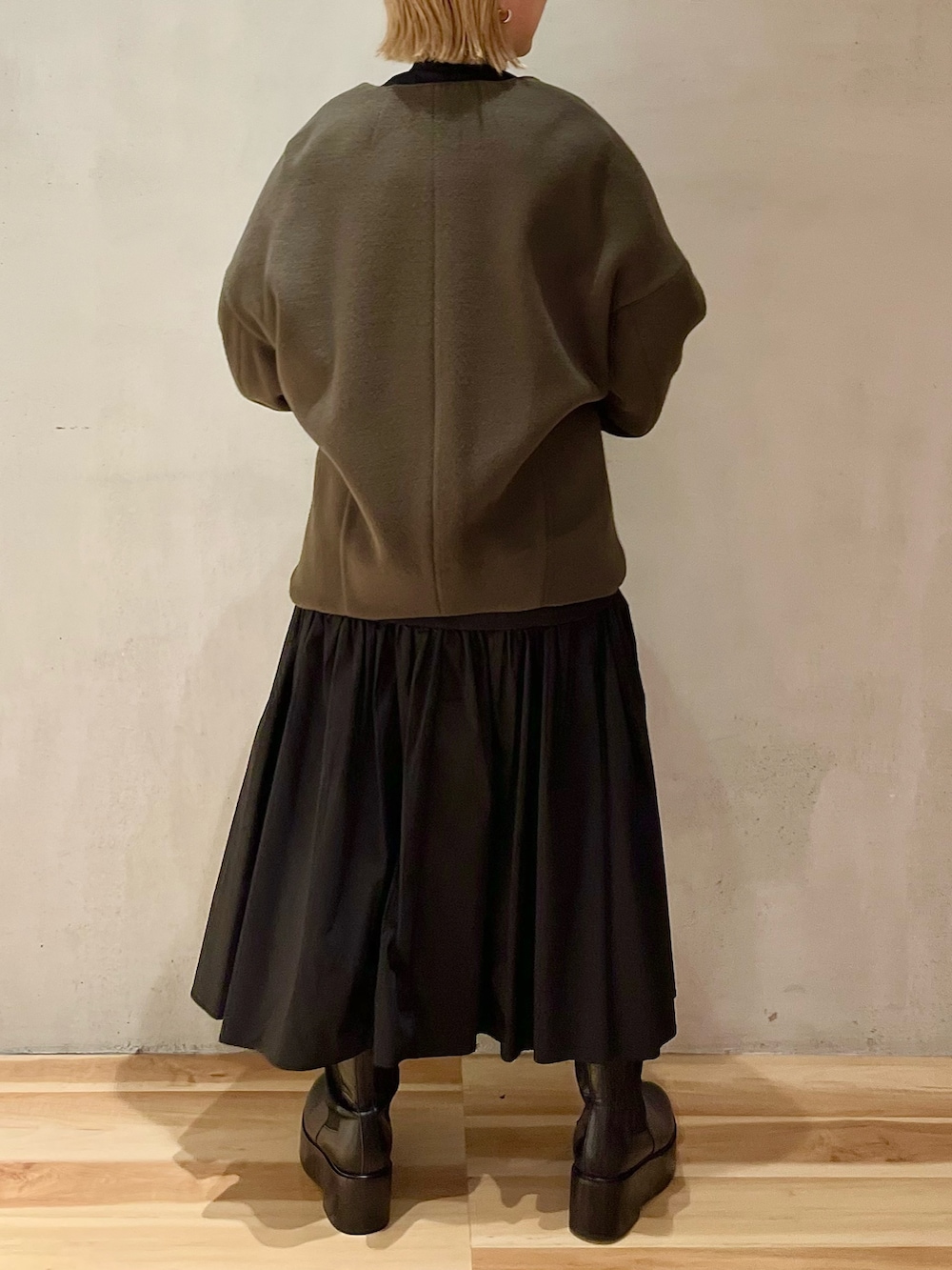 グリーン系のノーカラージャケット、ブラック系のワンピース、ブラック系のブーツを着用したレディースの秋コーディネートの3枚目の写真