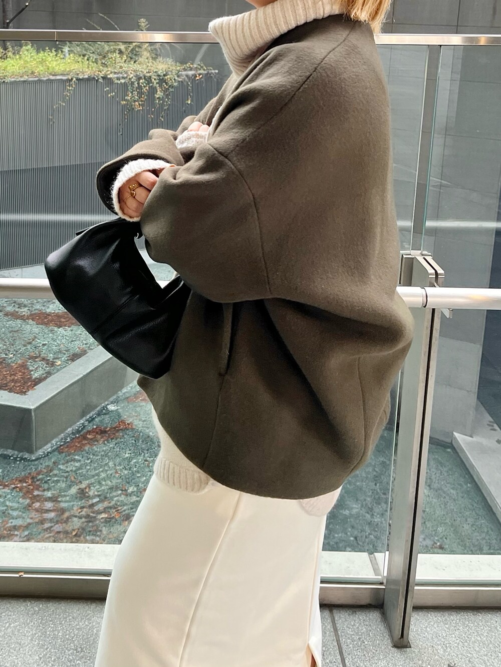 グリーン系のノーカラーコート、ブラック系のブーツを着用したレディースの冬コーディネートの6枚目の写真