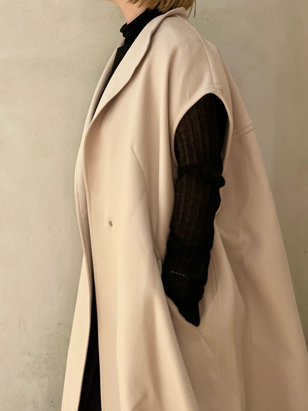 ベージュ系のノーカラーコート、ブラック系のニット/セーター、ブラック系のブーツを着用したレディースの秋コーディネートの5枚目の写真