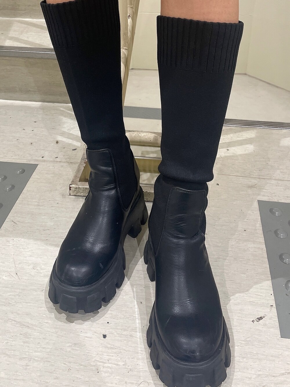 ブラック系のベスト、ブラック系のスカート、ブラック系のブーツを着用したレディースの秋コーディネートの7枚目の写真