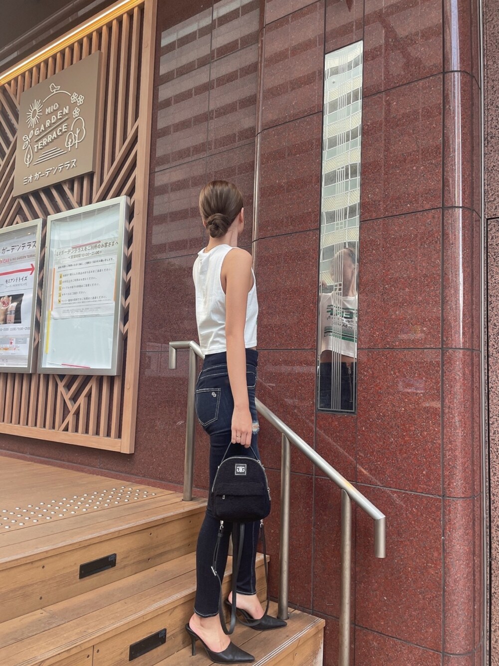 ホワイト系のタンクトップ、ブルー系のデニムパンツ、ブラック系のバックパック/リュックを着用したレディースの夏コーディネートの3枚目の写真