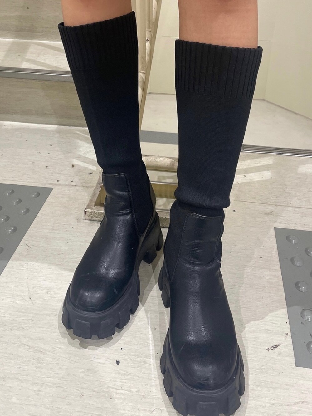 グレー系のニット/セーター、ブラック系のスカート、ブラック系のブーツを着用したレディースの秋コーディネートの7枚目の写真