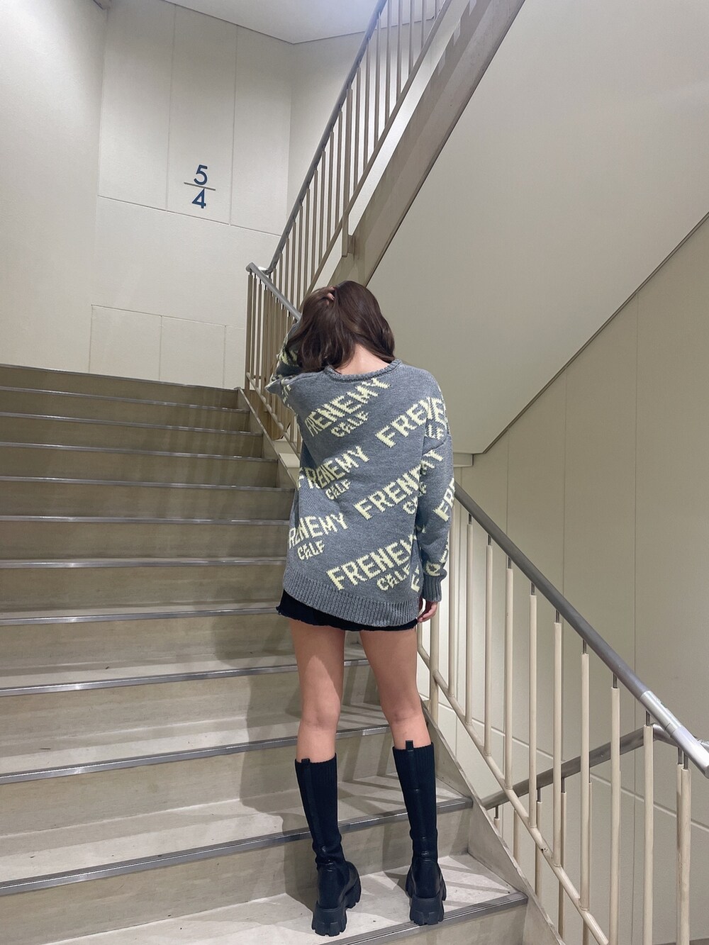 グレー系のニット/セーター、ブラック系のスカート、ブラック系のブーツを着用したレディースの秋コーディネートの2枚目の写真