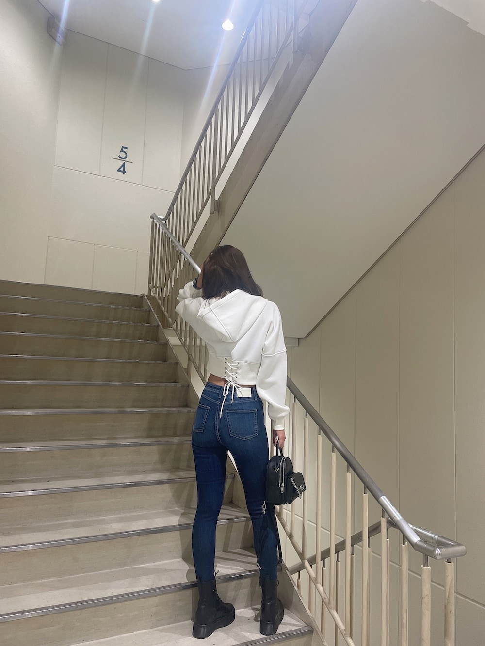 ブラック系のブーツ、ホワイト系のパーカー、ブルー系のデニムパンツを着用したレディースの秋コーディネートの2枚目の写真